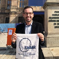 Porträtfoto Daniel Braga Nascimento. Er steht vor einem Universitätsgebäude und hält einen Beutel mit Aufschrift "EMMIR" in den Händen.