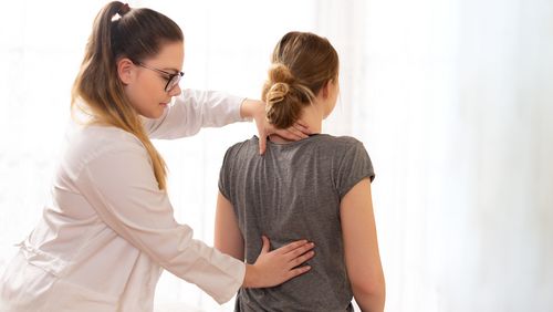 Physiotherapeutin tastet den Rücken einer Patientin ab.