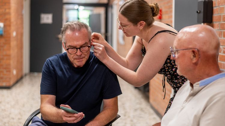 A young woman is attaching a small device to a middle-aged man's ear.