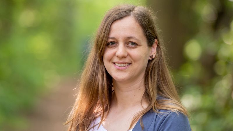Portrait einer jungen Frau mit langen Haaren vor einem unscharfen, grünen Hintergrund.