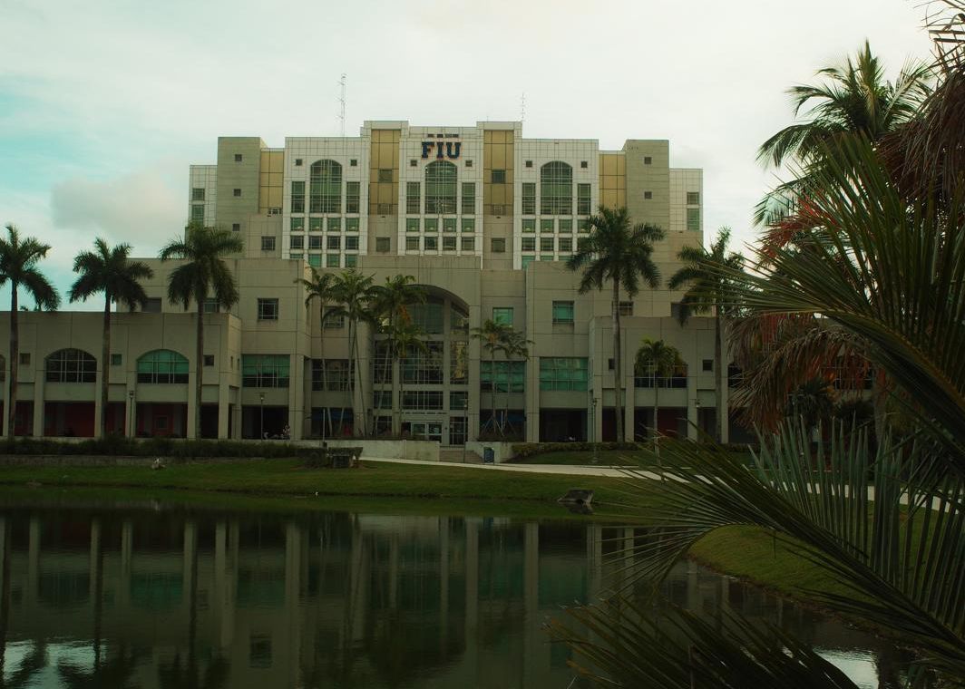 Modernes Bibliotheksgebäude mit Palmen, spiegelt sich in einem ruhigen See.
