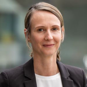 A portrait of Professor Gundula Zoch, wearing a white T-shirt and a black blazer, with honey-blonde hair tied back in a loose plait and parted at the side.
