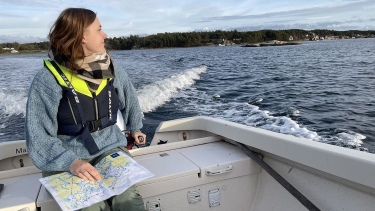 Junge Frau sitzt auf Motorboot und schaut zur Seite. Sie hält eine Karte in der Hand.