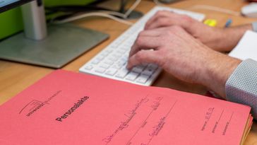 Hands on a keyboard, next to it is a personal file in paper form