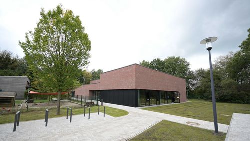 Frontalansicht des neuen Gebäudes. Es handelt sich um einen Klinkerbau mit Glasfront im Erdgeschoss. Im Vordergrund befinden sich Wege und Fahrradständer sowie mehrere Wiesenstücke