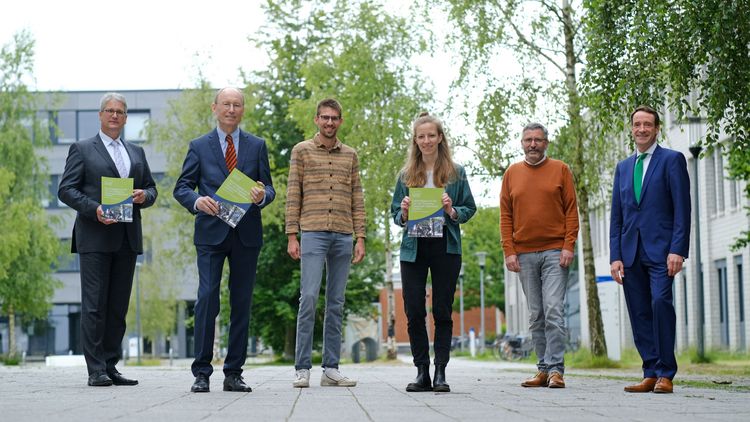 Die sechs Personen stehen etwas versetzt nebeneinander auf dem Campus, einige halten den Nachhaltigkeitsbericht in den Händen.