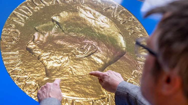 Das Bild zeigt Gunnar Zimmermann von hinten, während er mit seinen Fingern auf dem Multitouch-Tisch die Nobelmedaille bewegt. Zu erkennen ist das Porträt von Alfred Nobel.