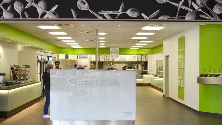 Der Eingangsbereich einer Cafeteria mit einem weißen Tresen und der Aufschrift "Cafeteria".