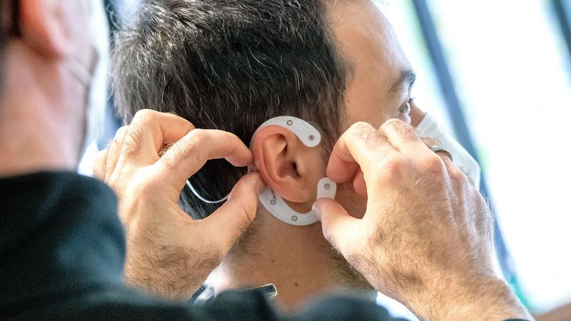 Martin Bleichner befestigt am Ohr einer anderen Person eine C-förmige Folie mit mehreren Elektroden.