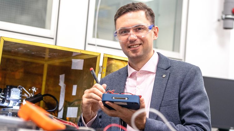 Dmitry Momotenko in the laboratory with protective goggles and a measuring device in his hand.