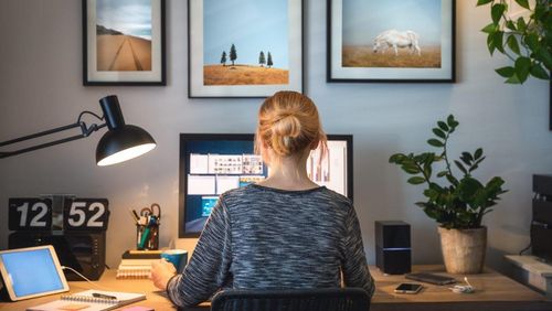 Foto, dass eine Frau von hinten am Schreibtisch sitzend im Homeoffice zeigt.