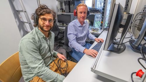 Bernhard Eurich und Mathias Dietz sitzen im Hörlabor vor einem Computer und tragen Kopfhörer.