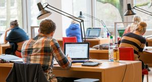 Eine Person sitzt in der Bibliothek an einem Tisch vor einem Laptop.