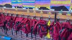 Ein Klassenraum oder Flur in einer Schule mit kindlichen Malereien von Bergen und einem Sonnenuntergang. Darunter hängen rote Schultaschen mit Lamas und Kindernamen.