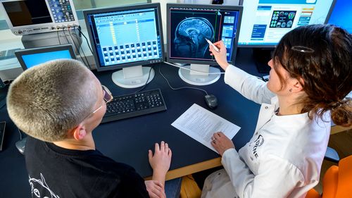 Two people sit in front of a monitor and watch a brain scan.