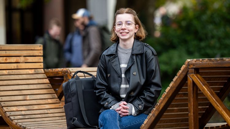 Eine junge Frau sitzt auf einer Holzbank und lacht in die Kamera.