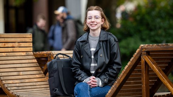 Eine junge Frau sitzt auf einer Holzbank und lacht in die Kamera.