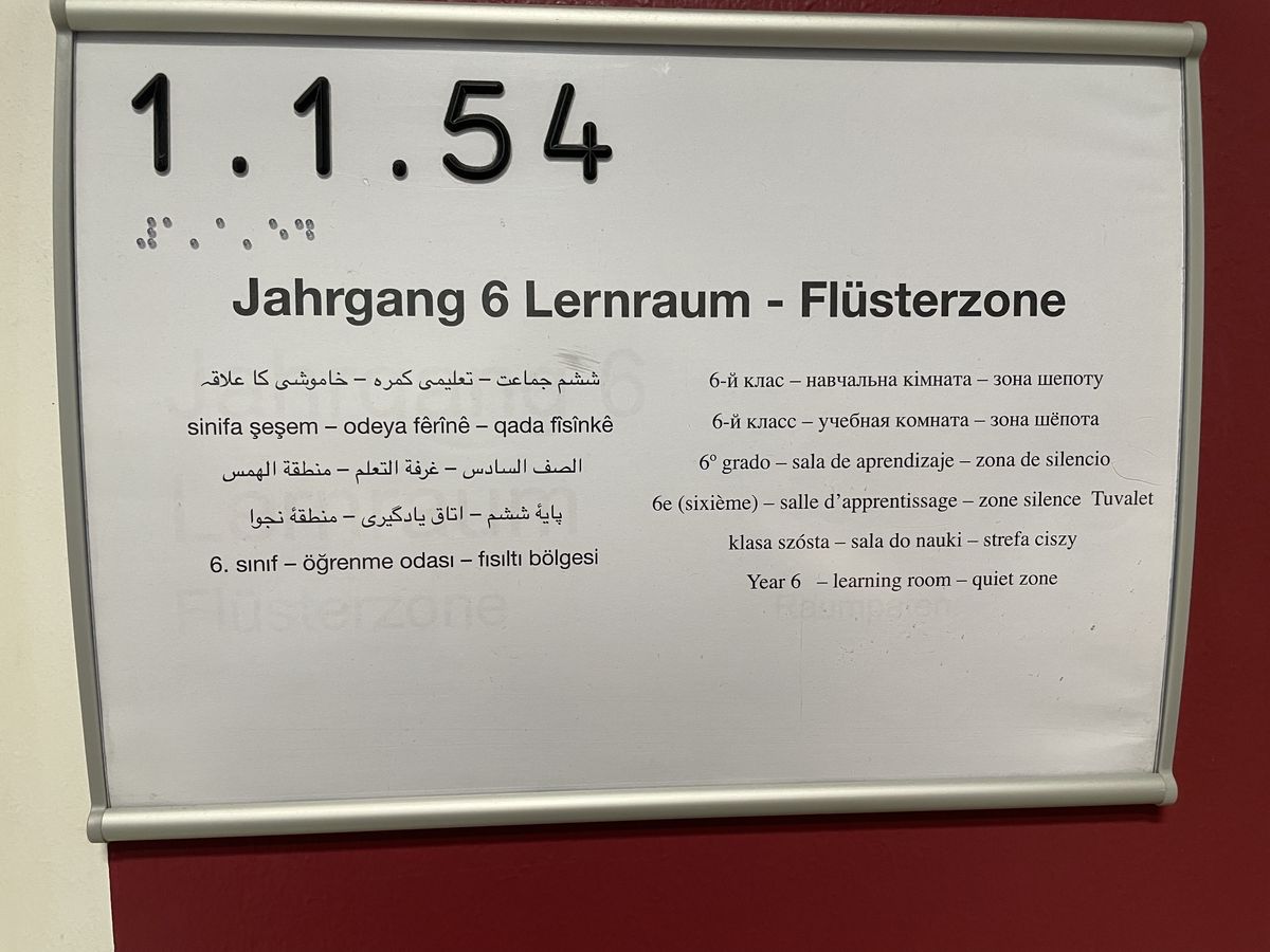 Beschilderung eines Lernraums an der IGS Flötenteich auf 12 Sprachen und Raumnummer auf Brailleschrift