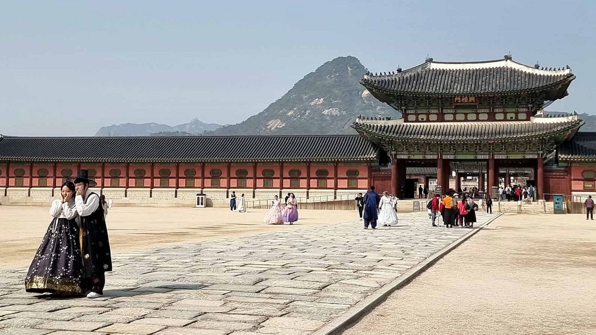 Der Gyeongbokgung Palast in Seoul mit traditionellen Gebäuden und Besucher*innen in Hanboks.
