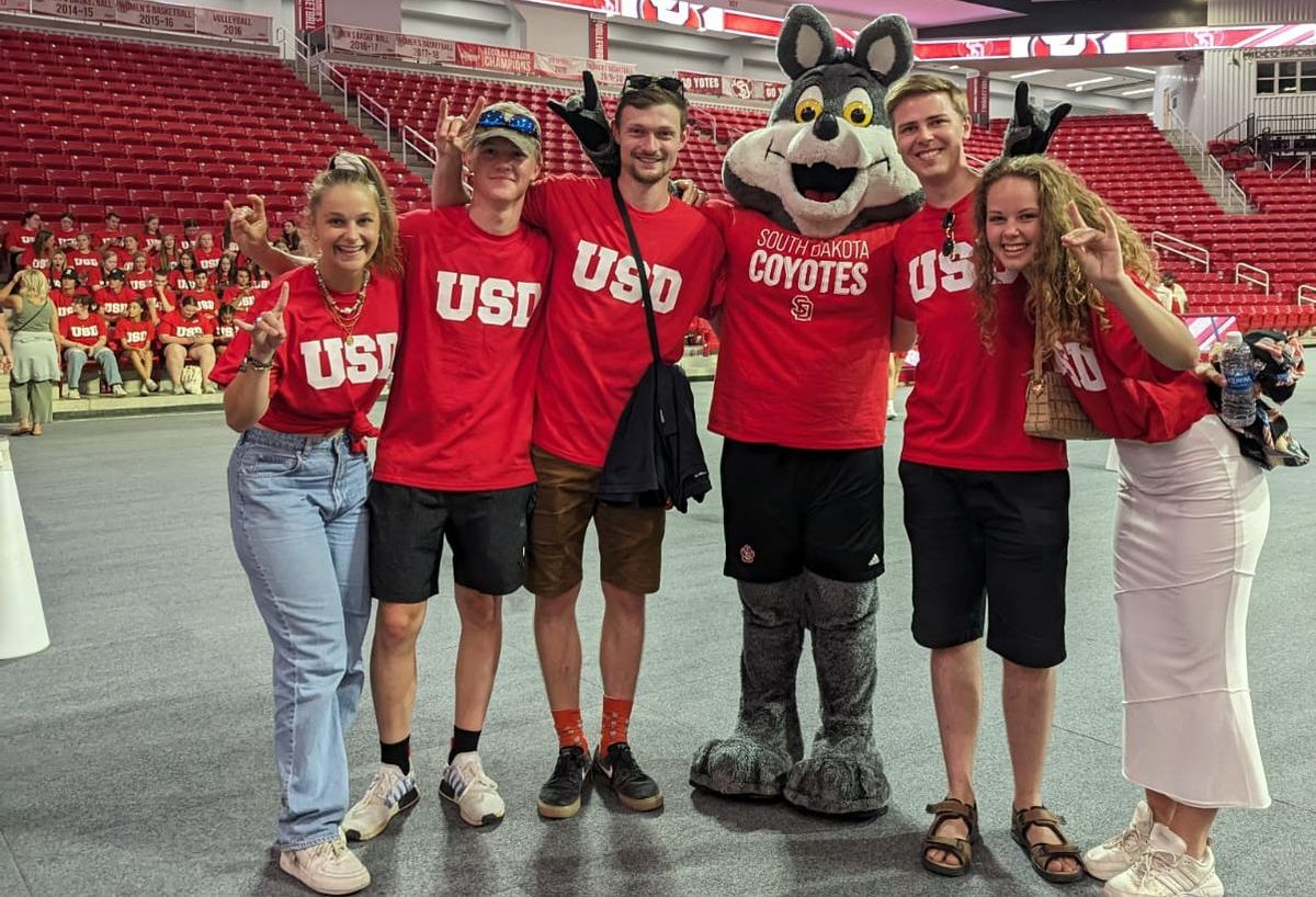 Gruppe von Menschen posiert mit dem Maskottchen der South Dakota Coyotes.