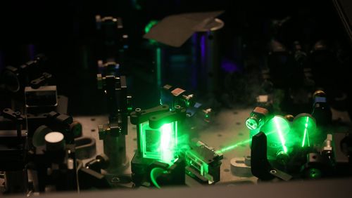 A green laser beam is guided by mirrors and lenses through an experimental set-up.