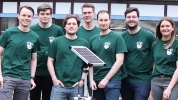 Sieben junge Erwachsene tragen dunkelgrüne T-Shirts mit einem weißen Logo, das einen Deich zeigt. Darüber die Aufschrift Diek un Dat.