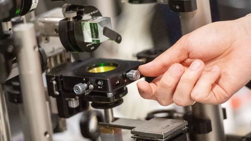 A hand turns a screw on an experimental setup.