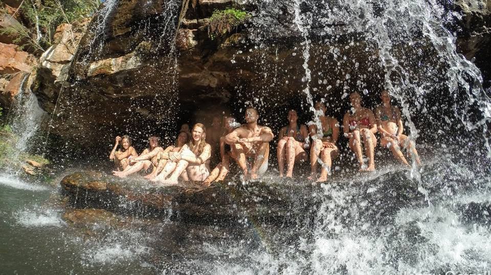 Eine Gruppe Menschen sitzt hinter einem Wasserfall in einem natürlichen Becken.