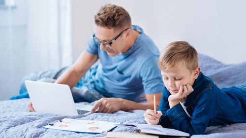 Vater am Laptop, Kind macht Hausaufgaben