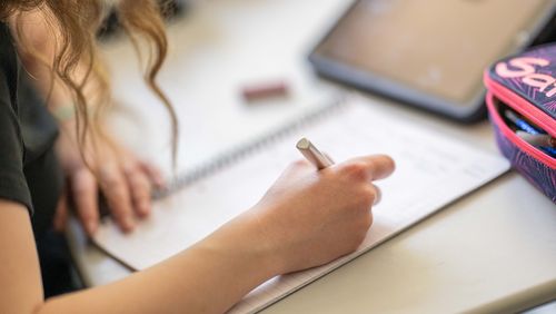 Schülerin schreibt in ein Heft, Großaufnahme der Hand mit Stift. 