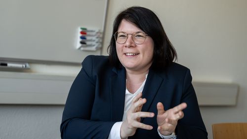 Das Bild zeigt Dörte Dannemann. Sie sitzt dem Interviewer gegenüber und spricht gerade. Dabei lächelt sie und gestikuliert leicht mit ihren Händen. Im Hintergrund des Büros ist eine Flipchart zu erkennen.