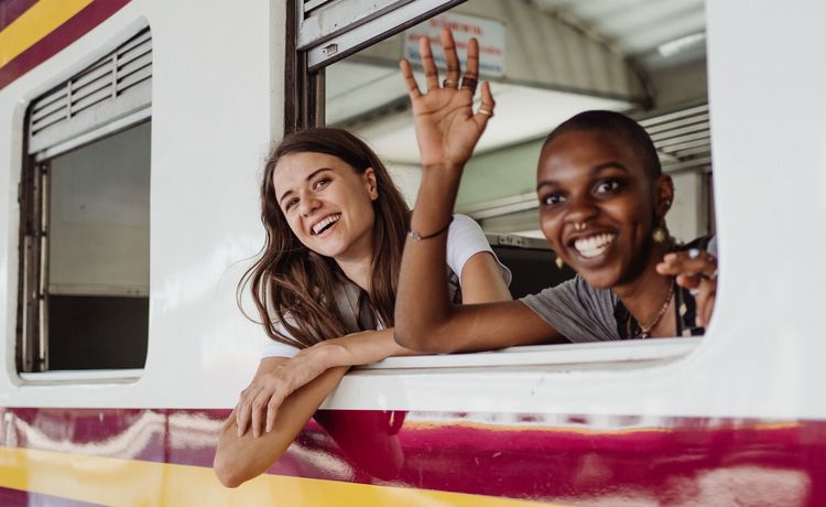Two smiling people waving from a train window.