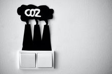 Above two white light switches, three chimneys with a cloud coming out of them are stuck on with black cardboard. CO2 is written in white in this cloud.