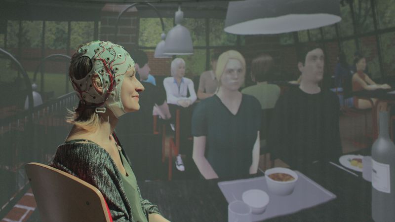Junge Frau mit EEG-Haube, im Hintergrund virtuelle Mensa-Umgebung.