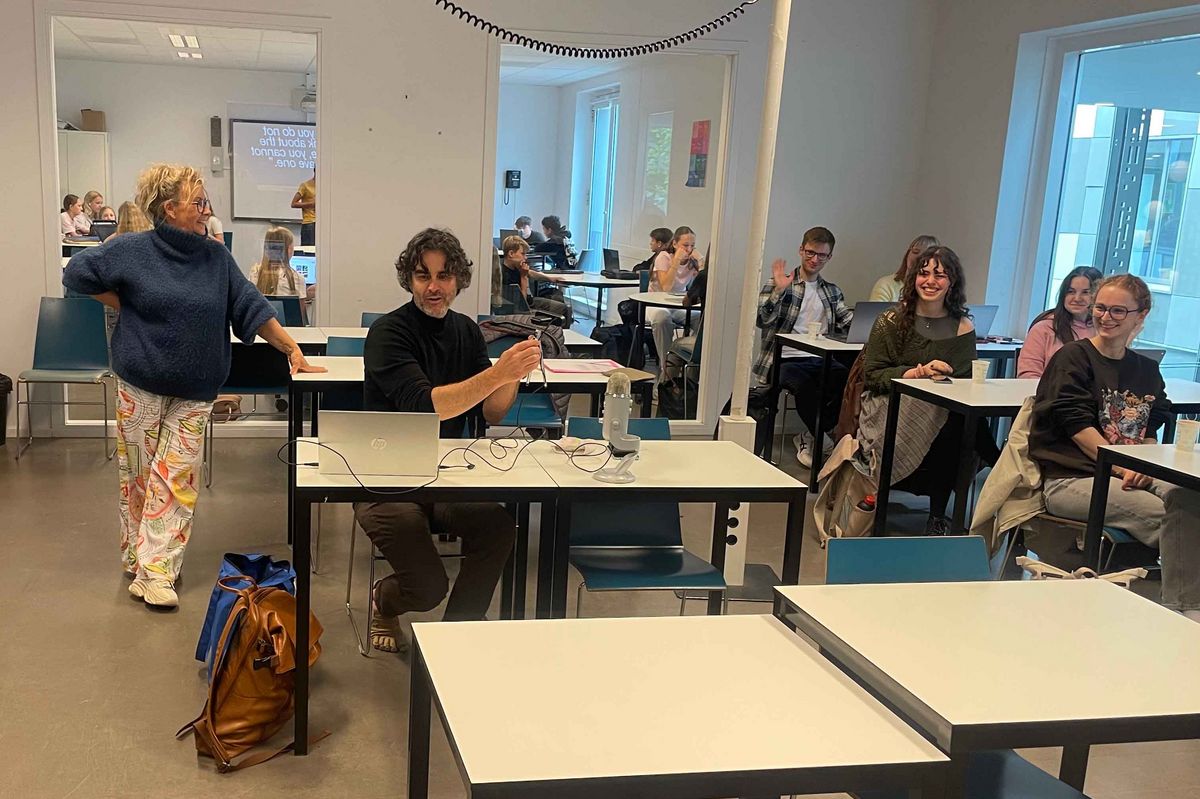  classroom in the Schule Stad&Esch with people working or chatting at tables. A man with laptop in the foreground.