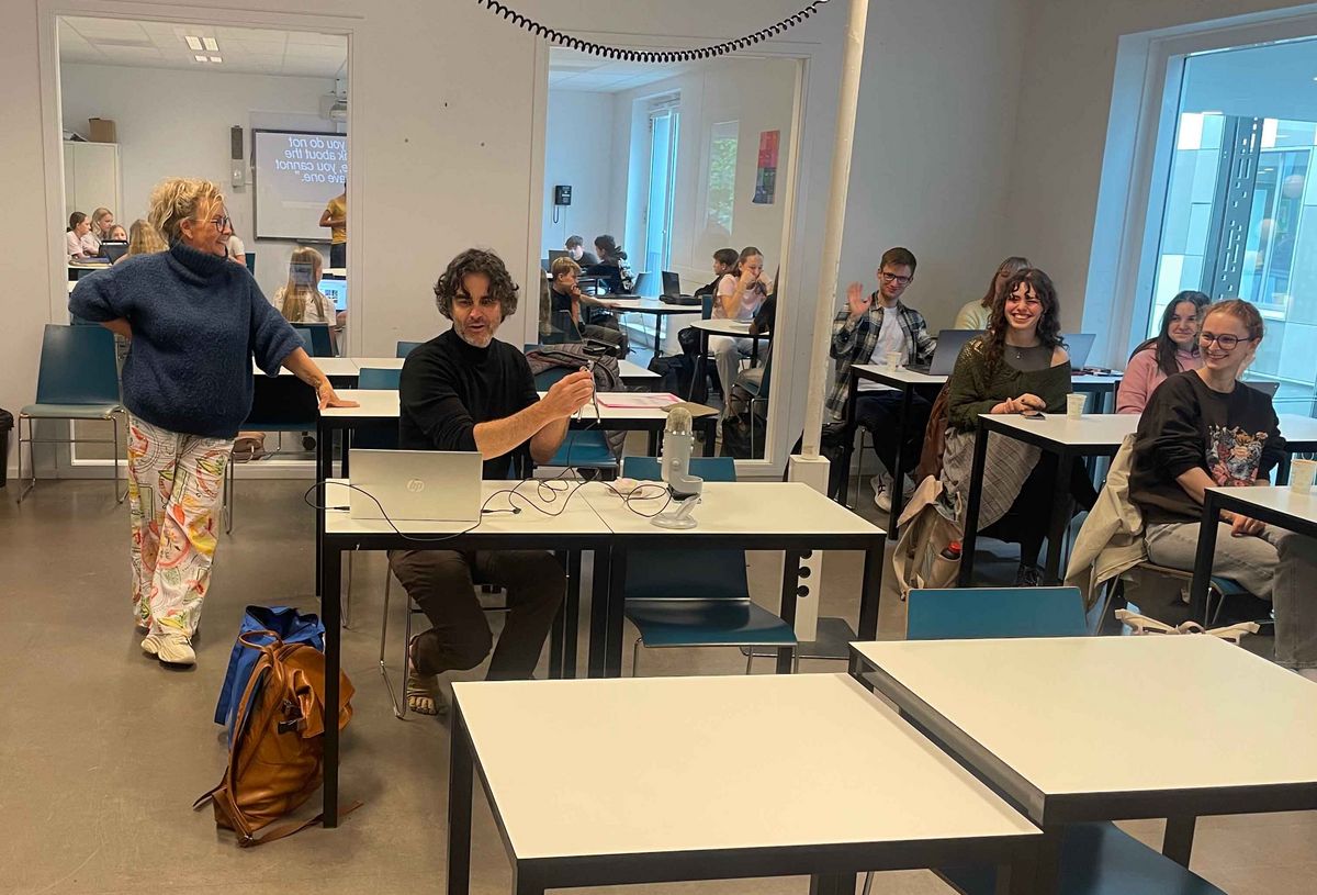 Ein Klassenzimmer in der Schule Stad&Esch mit Menschen, die an Tischen arbeiten oder sich unterhalten. Im Vordergrund ein Mann mit Laptop.
