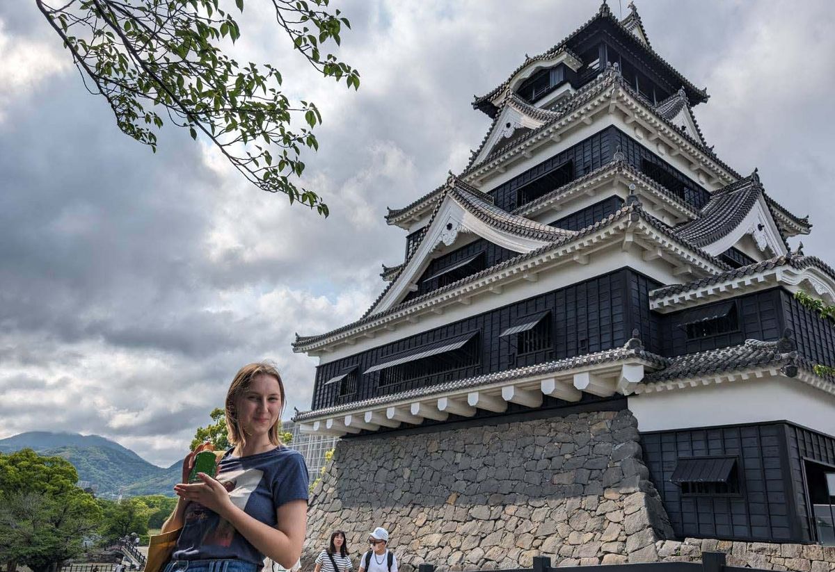 Kumamoto Castle, a multi-storey castle with dark wooden outer walls and a person in the foreground.