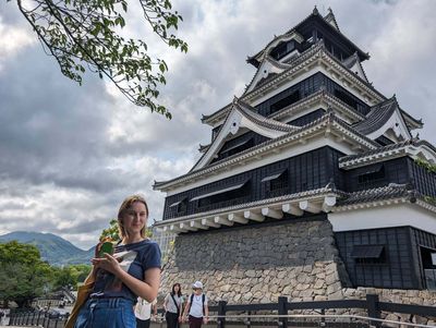 Burg Kumamoto, eine mehrstöckige Burg mit dunklen Holzaußenwänden und einer Person im Vordergrund.
