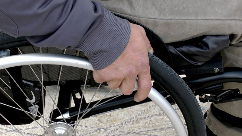 Großaufnahme einer Hand am Rad eines Rollstuhls.