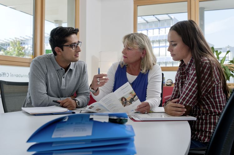 Drei Personen sitzen an einem Tisch und besprechen Unterlagen.