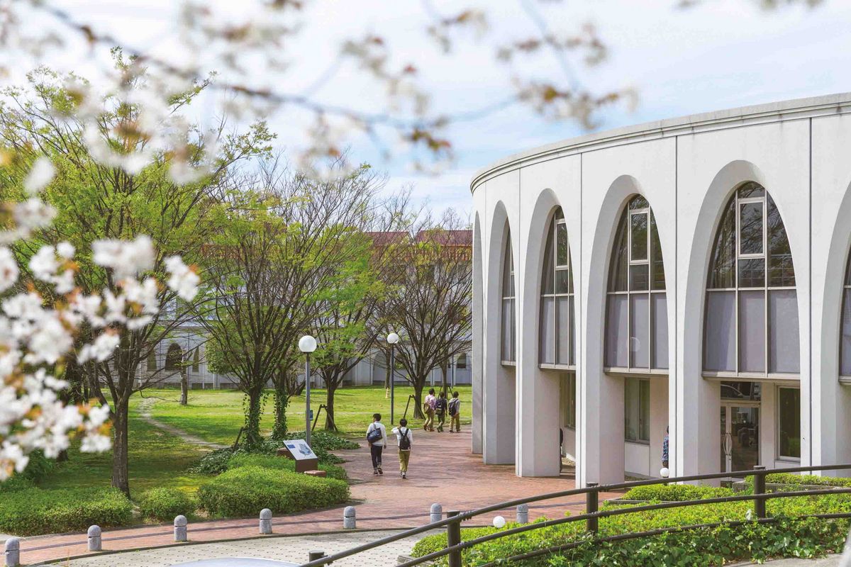 Ein Gebäude auf dem Nagoya Campus mit gebogener Fassade und Arkaden, mit Blütenzweigen im Vordergrund.