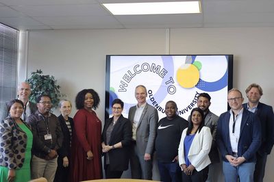 Eine Gruppe von zwölf Personen posiert vor einem Schild mit dem Text "WELCOME TO OLDENBURG UNIVERSITY". 