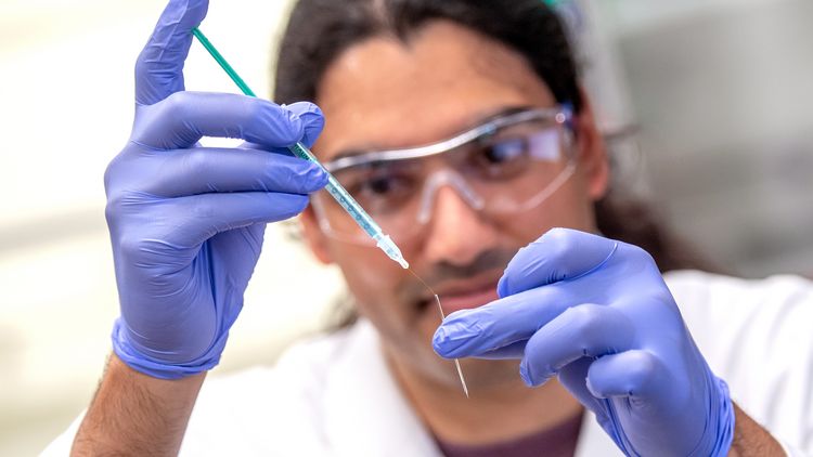 A scientist has a narrow pipette in his hand with which he places a hair-thin wire in the printing nozzle made of glass. 
