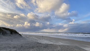Blick vom Strand Richtung Meer, dramatische Wolken türmen sich am Himmel. 