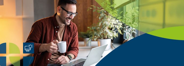 A man holds a coffee cup and looks at a laptop.