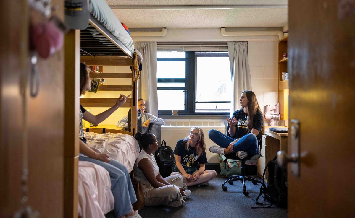 Studierende sitzen in einem Studierendenwohnheim zusammen und unterhalten sich. Ein Zimmer mit Etagenbett und Schreibtisch.