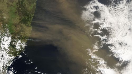 Satellitenbild zeigt die Australische Küste, den Pazifischen Ozean, einige weiße Wolken und die bräunliche Staubwolke. 