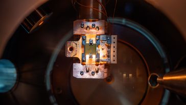 Großaufnahme einer etwa 1cm mal 1cm großen Probe, die in eine Halterung eingespannt ist und sich in der Vakuumkammer befindet. 