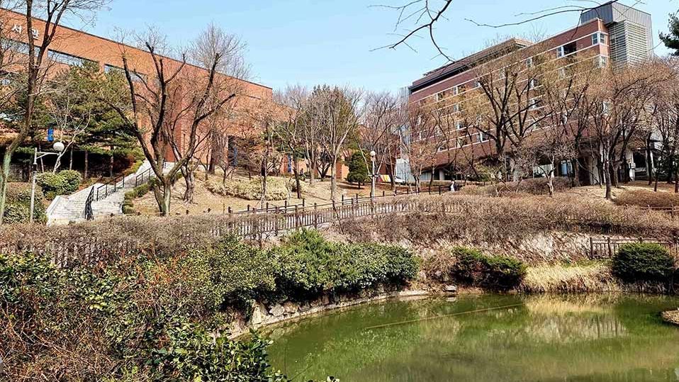 Der Campusteich der University of Seoul mit grüner Vegetation und modernen Gebäuden im Hintergrund.