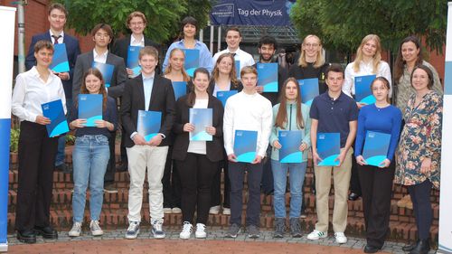 The picture shows prize winners standing at the entrance to the Wechloy campus. They hold their certificates in their hands and look into the camera.